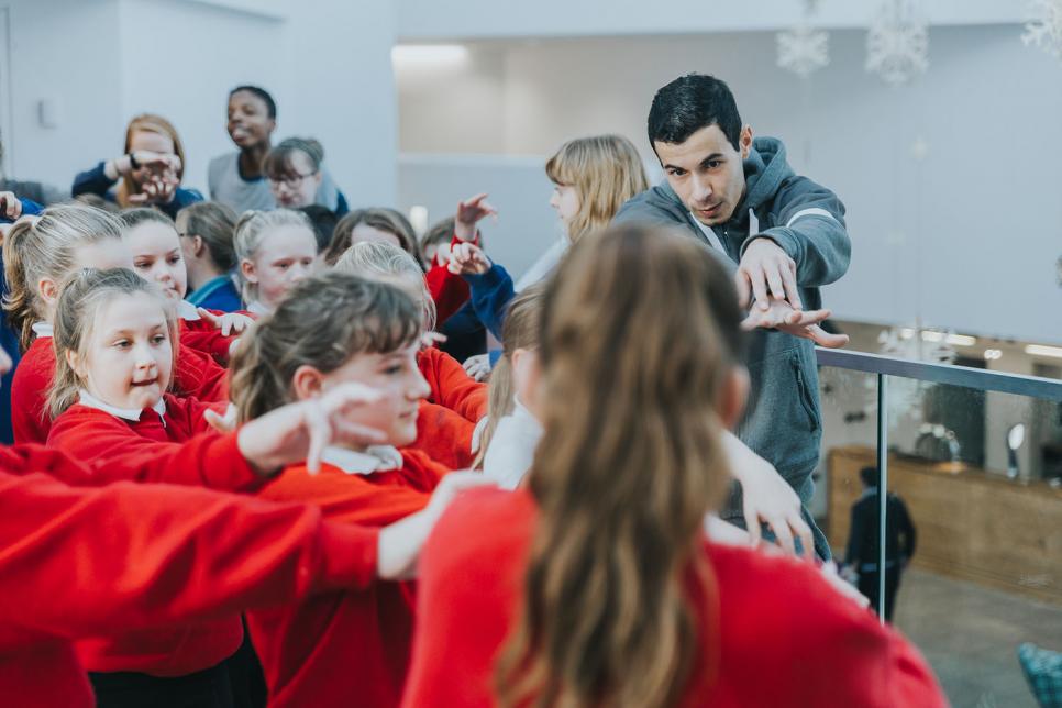 Man conducting a creative workshop with children in red jumpers
