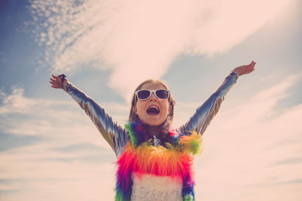 Young girl dressed in a colourful costume with her hands in the air.