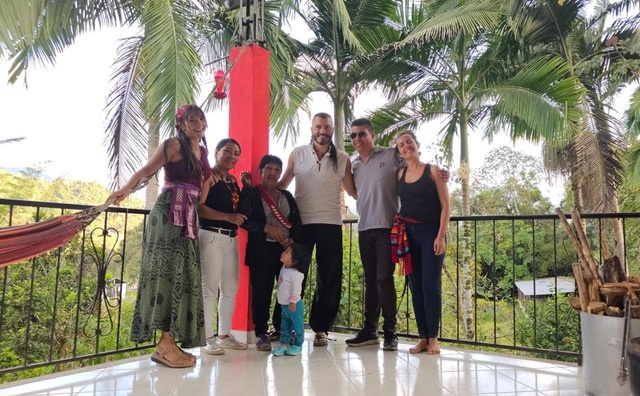 6 individuals standing on a balcony with black metal bars with palm trees in the background