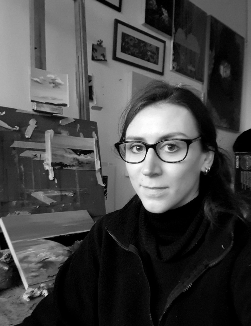Tessa Gray A lady in glasses smiling in an art studio, in black and white.